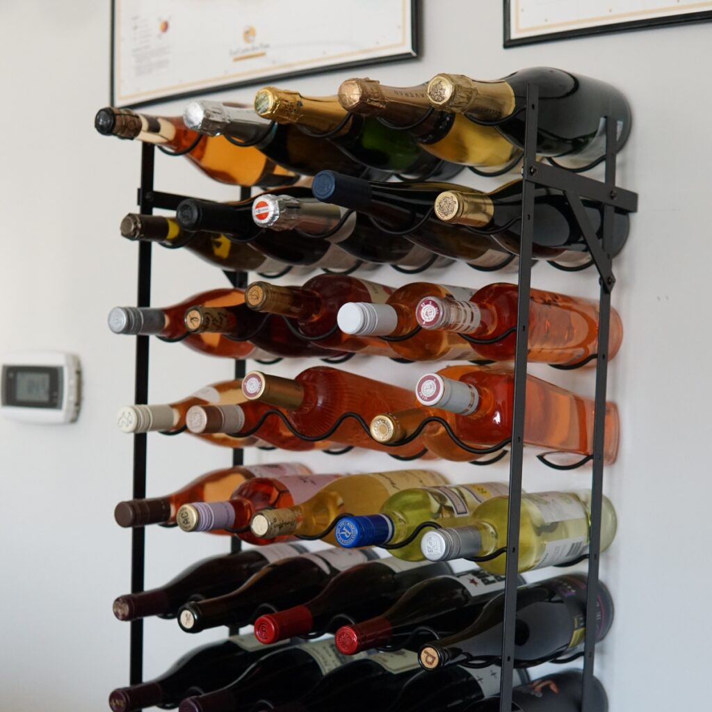 close-up view of a tall, black metal wine rack filled with various bottles of wine placed against a white wall